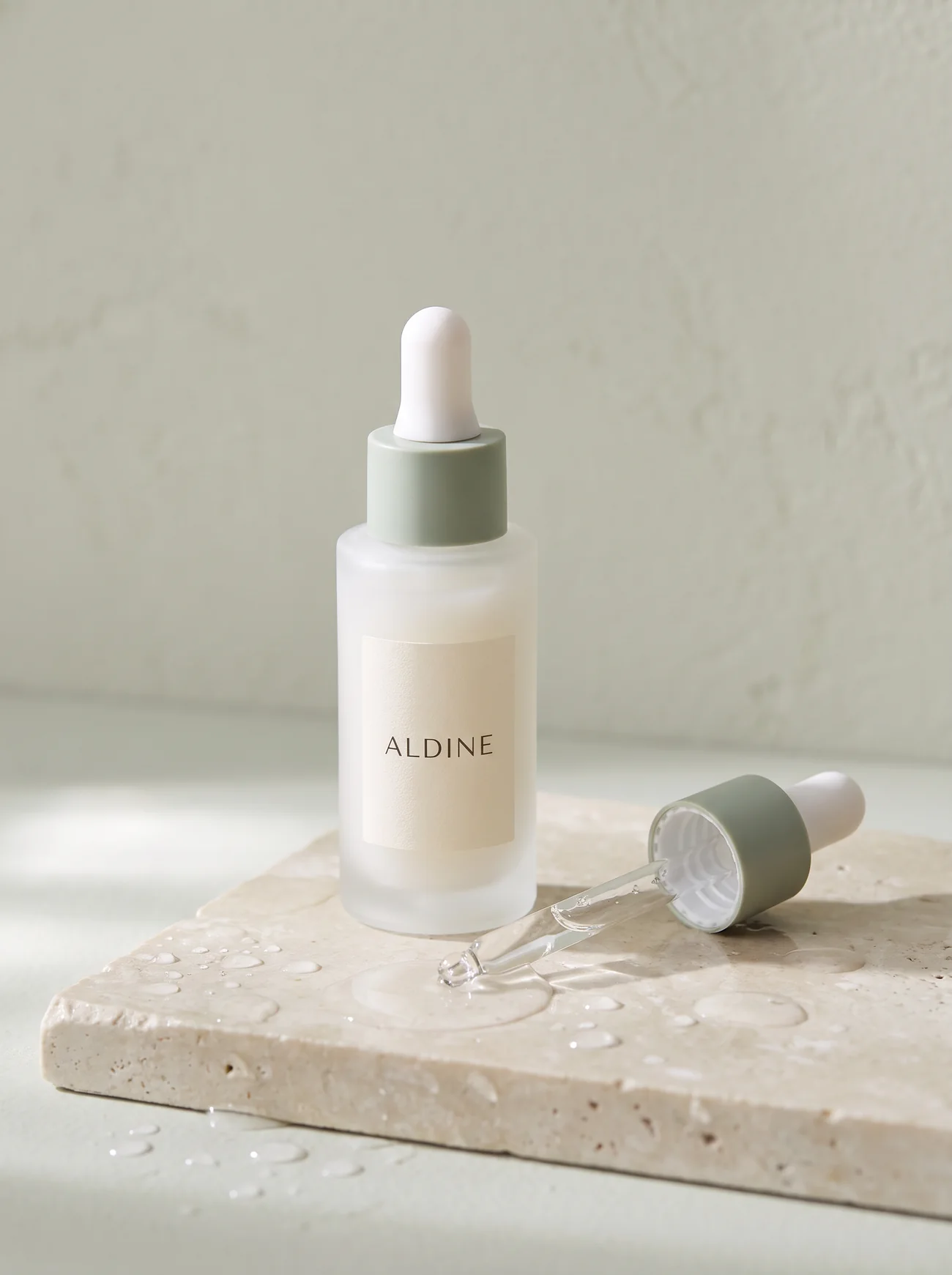 A frosted glass dropper bottle on wet stone with a bead of serum