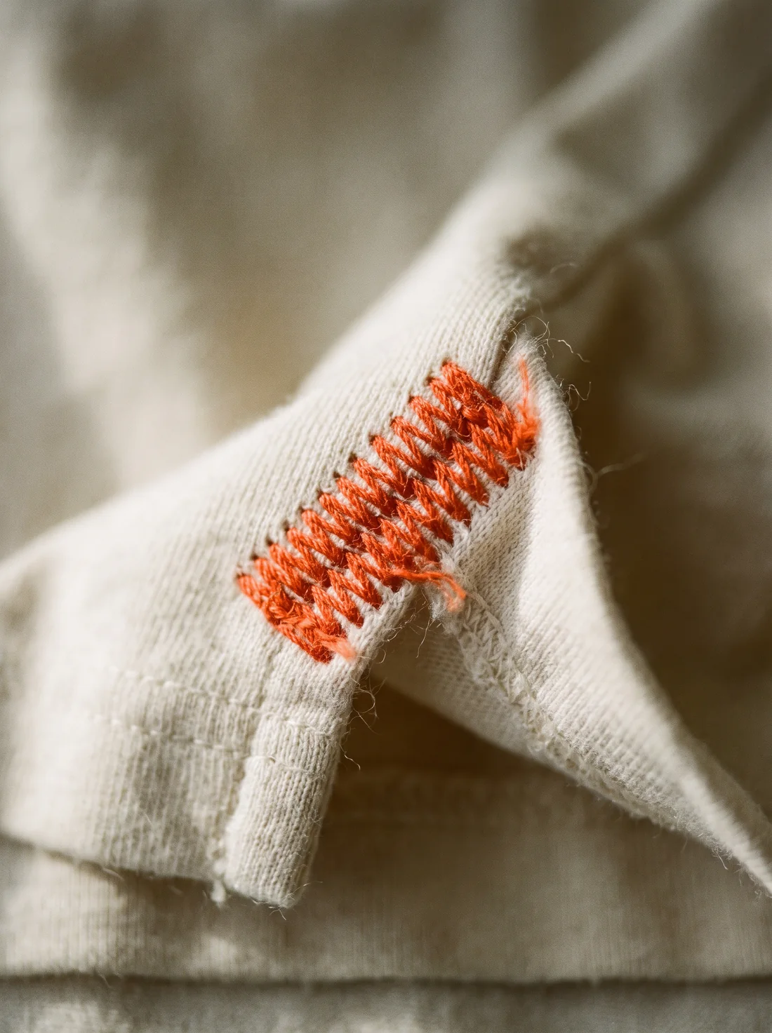 A macro photograph of dense orange bartack stitches at the corner of a garment