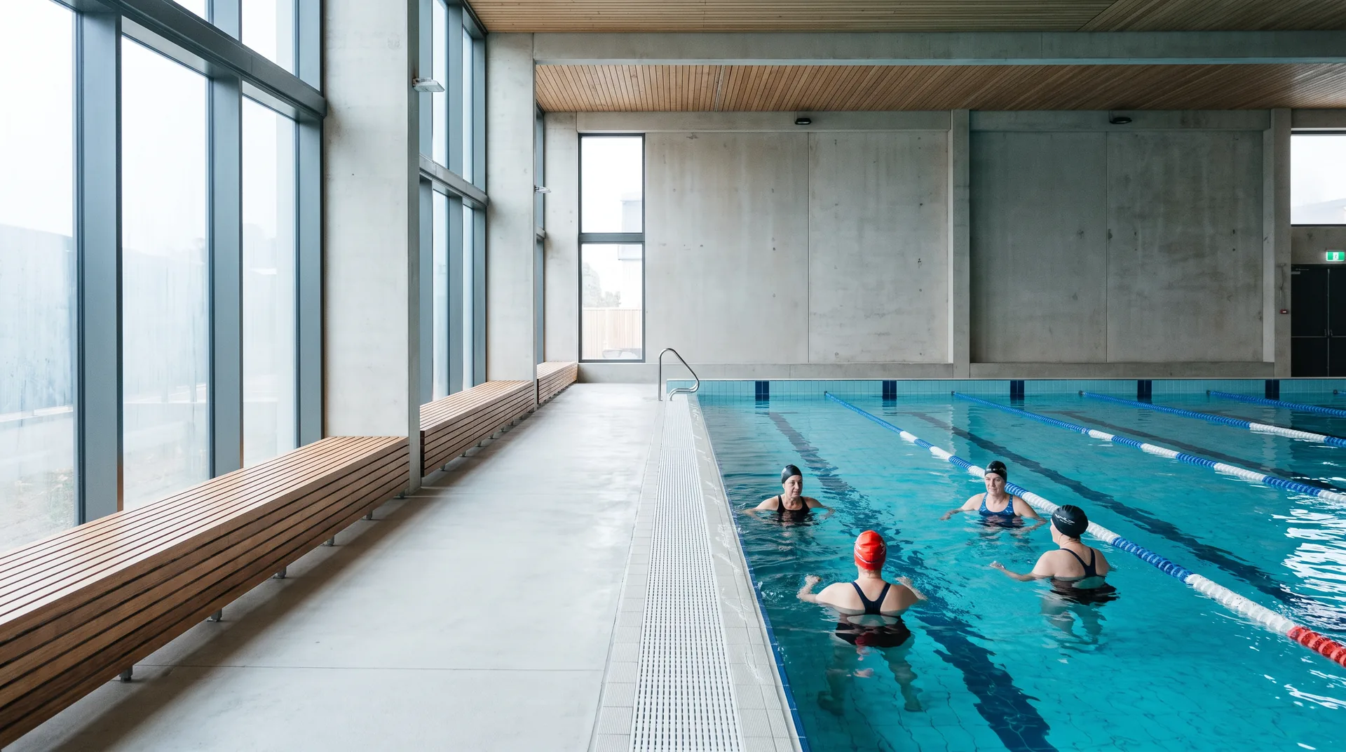 A 25 metre indoor pool with swimmers in the shallow end and tall windows along one side