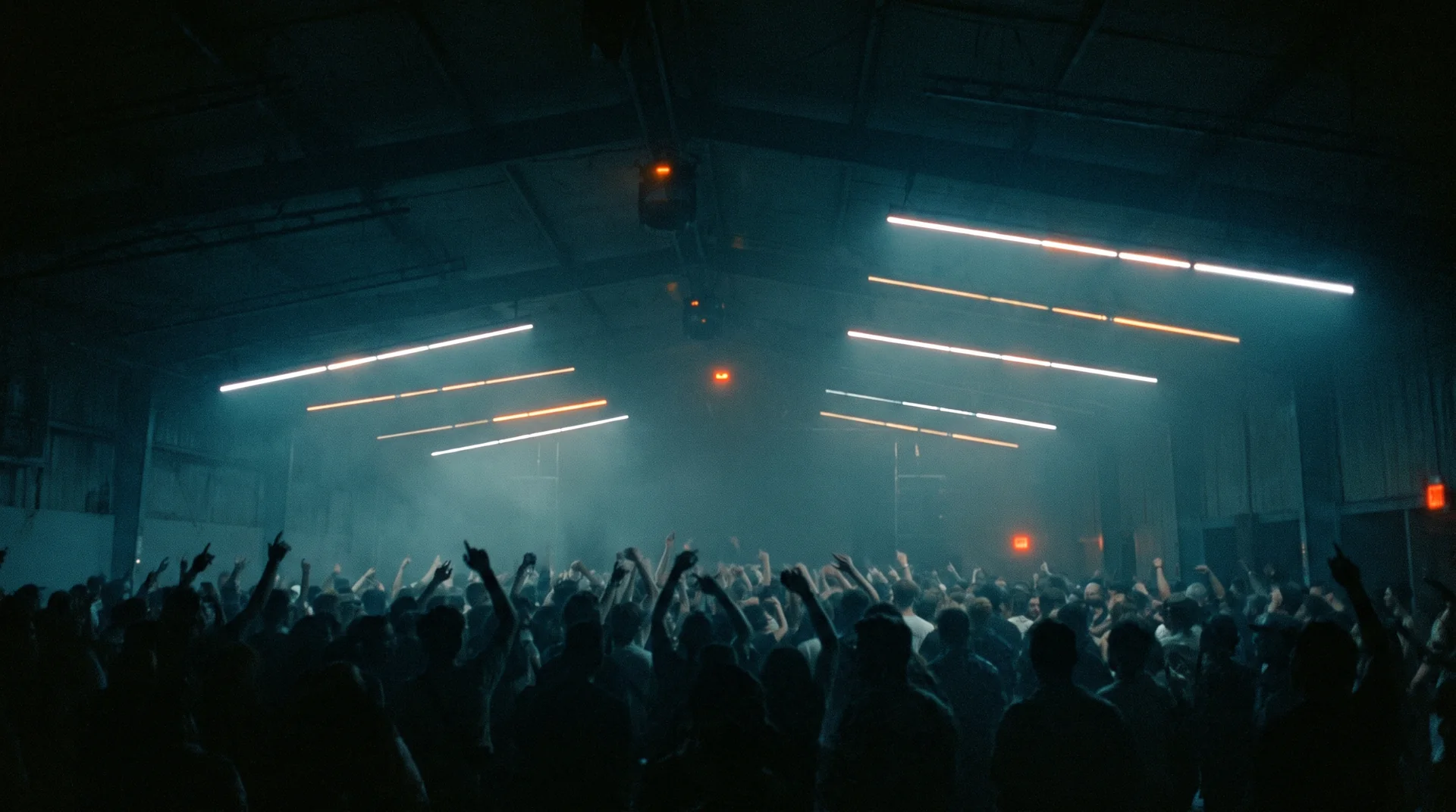 Silhouettes of a crowd with raised hands in front of rows of light bars and haze
