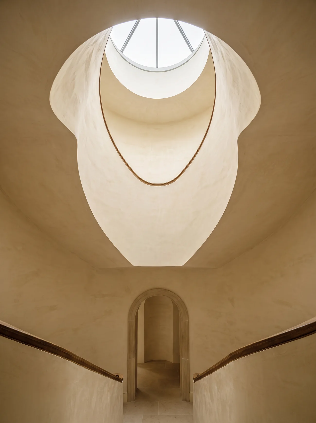 A spiral staircase in pale lime plaster with an oak handrail under a round rooflight