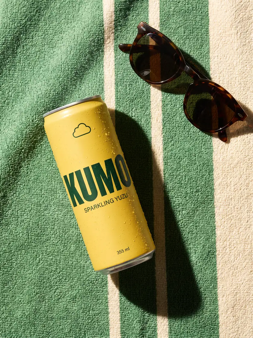 A can of Kumo on a striped beach towel next to sunglasses