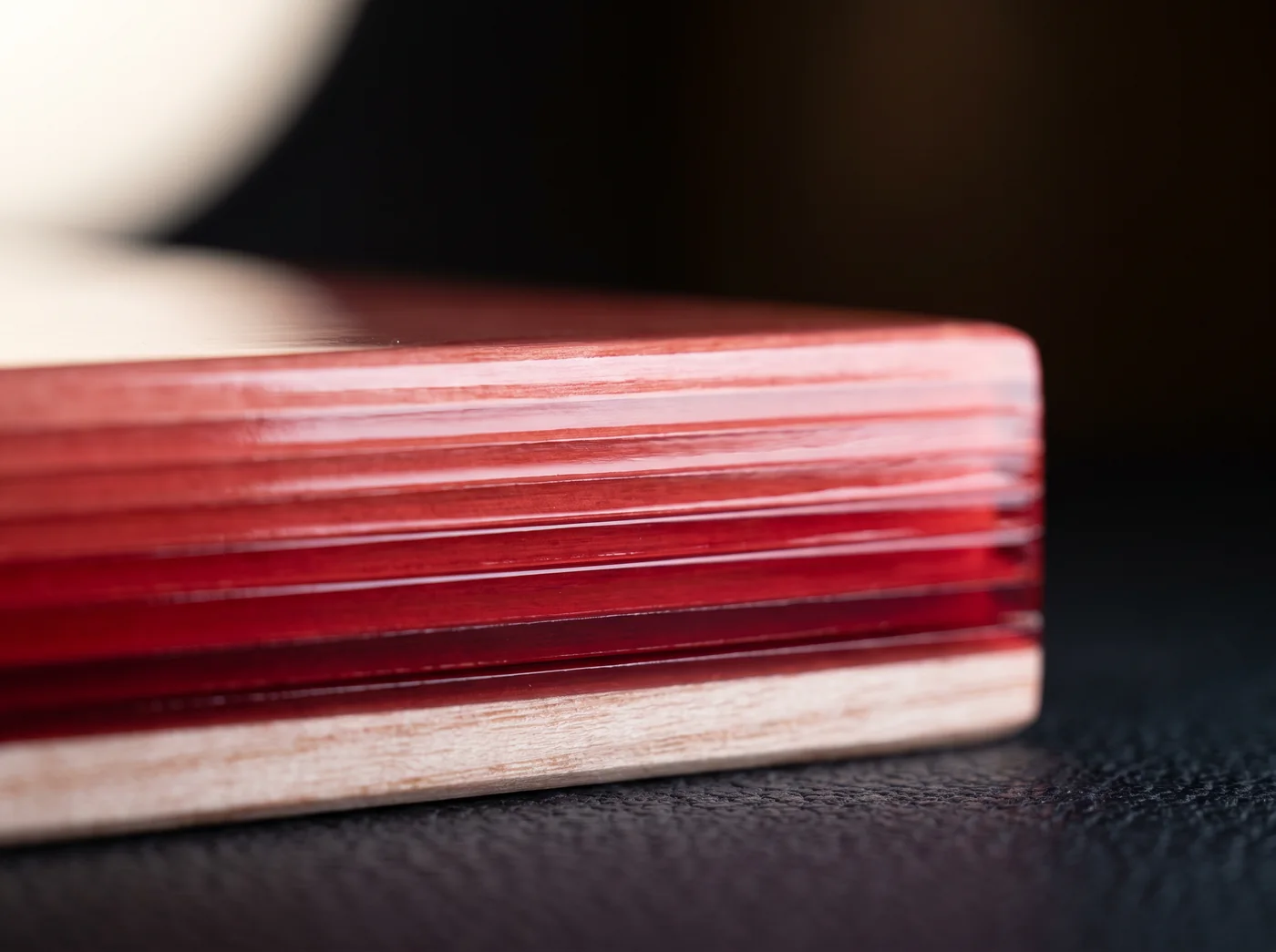 The cut edge of a lacquered board showing seven layers of red lacquer over pale grain