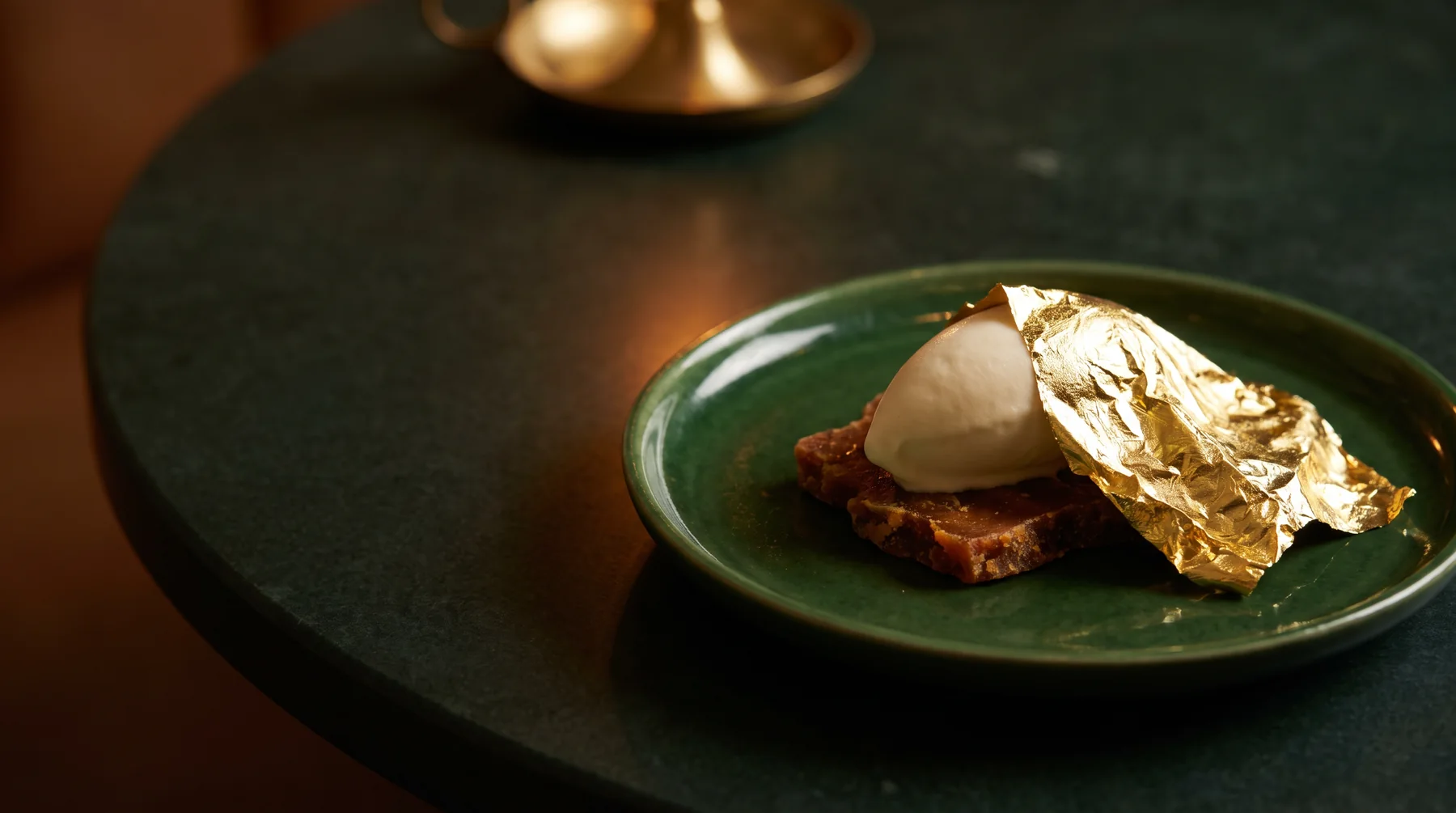A quenelle of buttermilk ice cream under a sheet of gold leaf on a green plate
