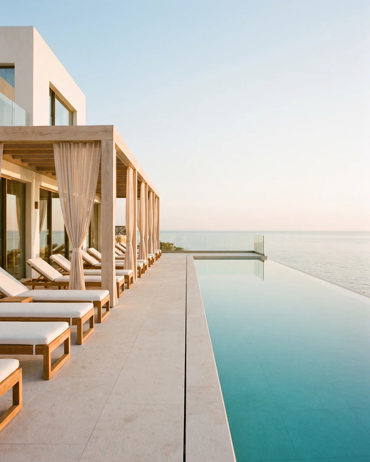 An infinity pool that runs to the horizon beside a pale oak pergola and teak loungers