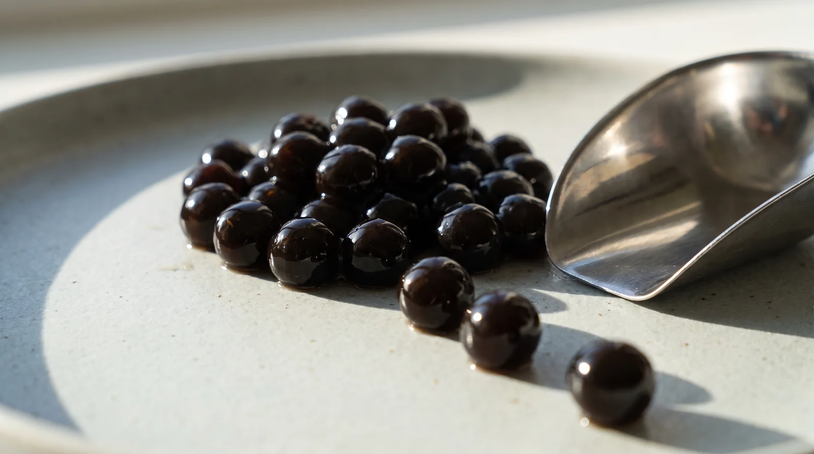 A heap of glossy black tapioca pearls with a steel scoop lifting a few from the pile