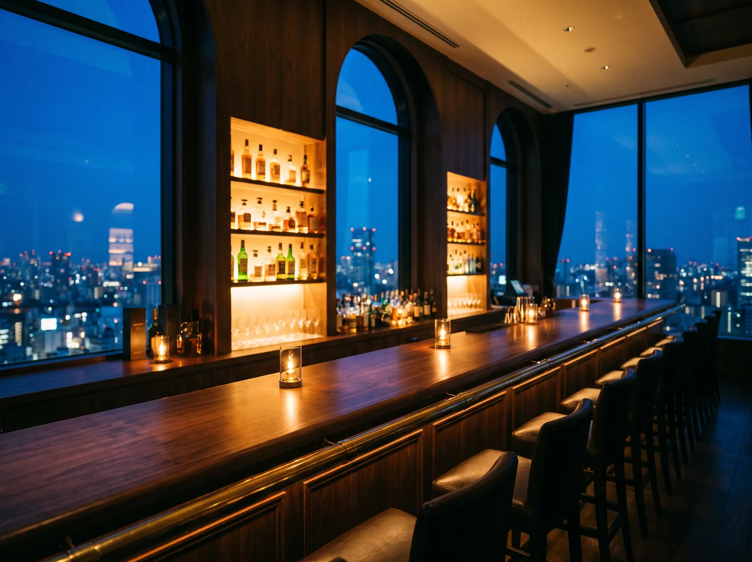 The bar room with a long walnut counter, backlit shelves and arched windows onto the night