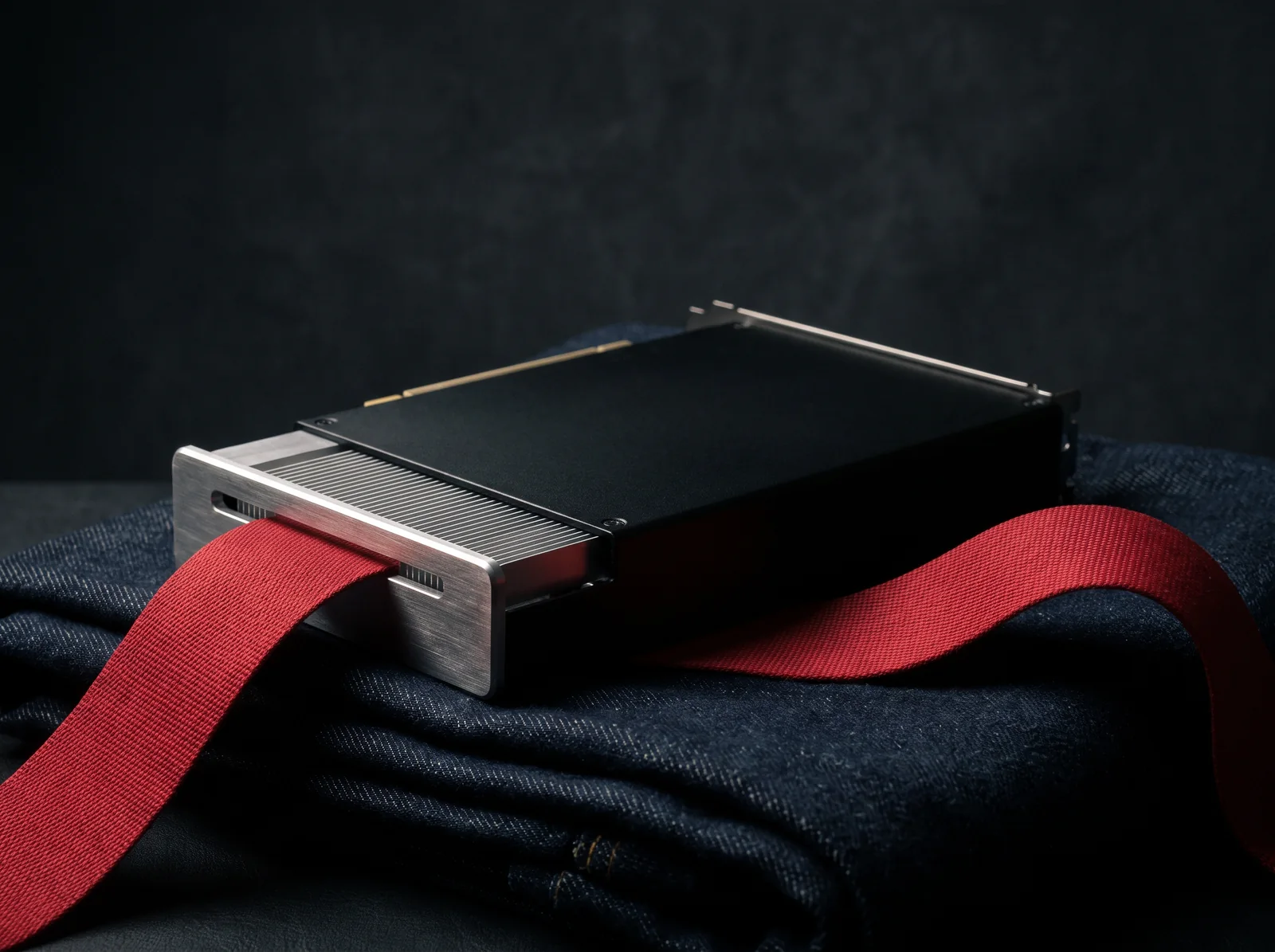 A GPU accelerator card on folded raw denim with a wide red ribbon threaded through it