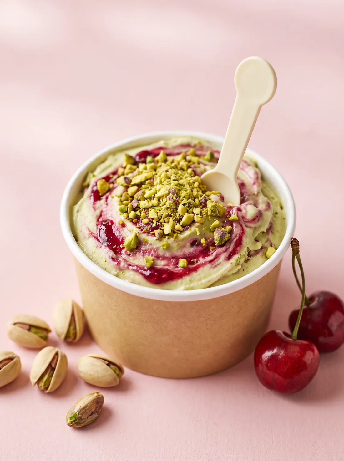 A cup of pistachio gelato with a sour cherry ripple and a small spoon