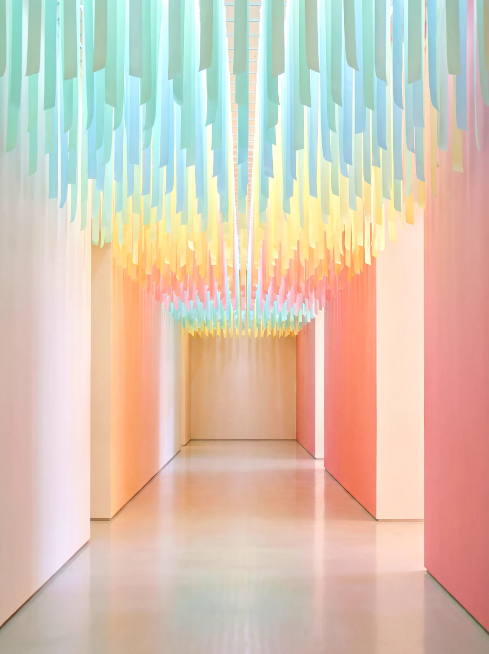 A tall narrow corridor of hanging translucent ribbons in mint, sky blue and butter yellow, backlit