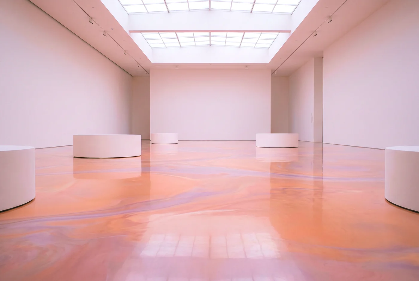 A hall whose floor is a sheet of marbled pastel liquid with a few white plinths standing in it