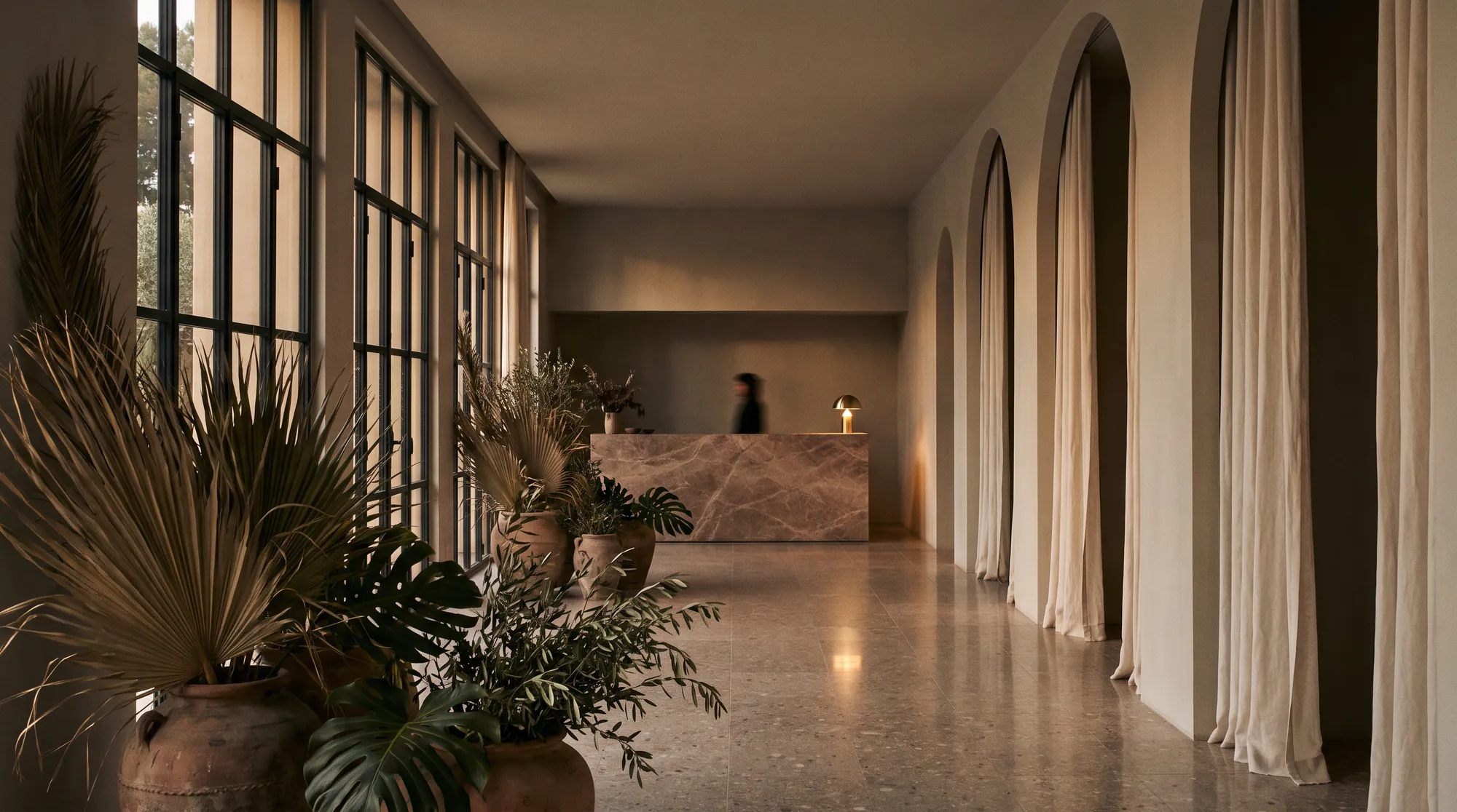 Tall steel-framed windows and dried palms at the near end of the hall